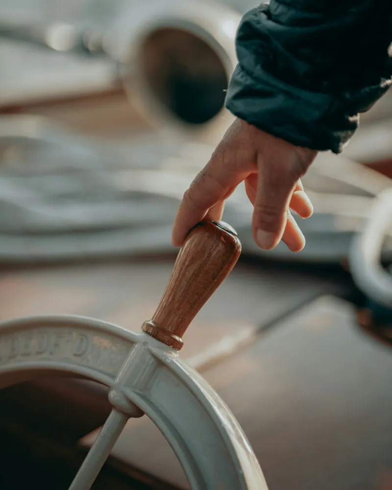 Une main posée sur la barre à roue d’un bateau.